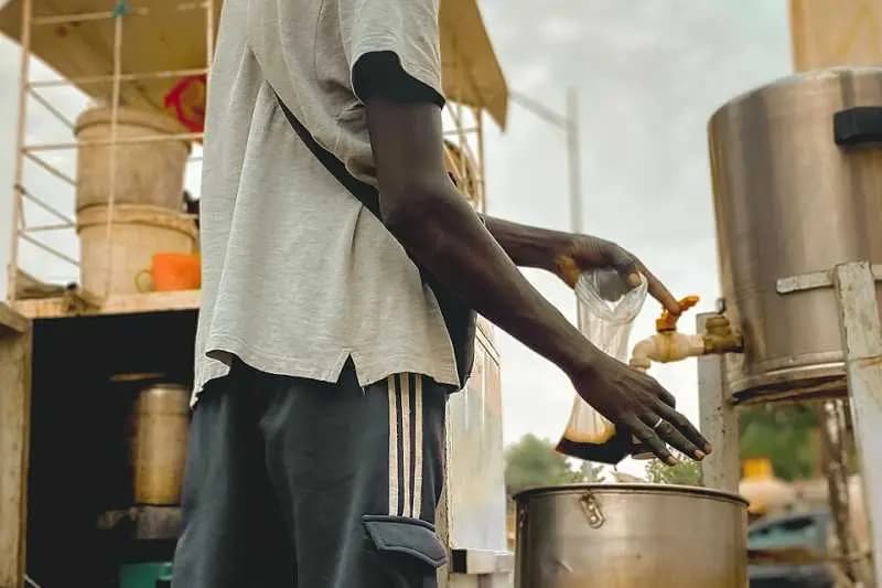 Vendeur de rue remplissant un sachet de café Touba au robinet d'une grande marmite