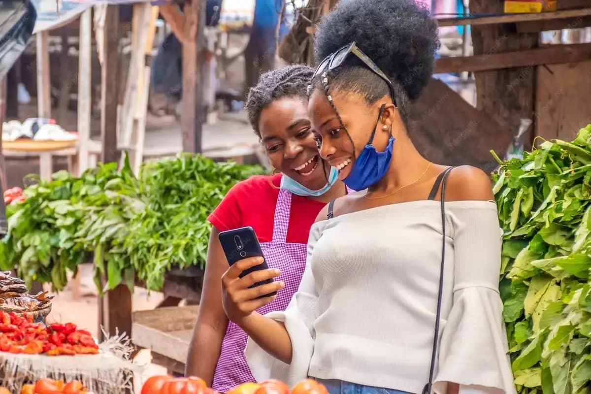 Deux commerçantes consultent un téléphone sur un marché