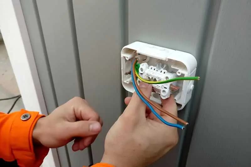 Électricien raccordant les fils d'une prise électrique, dont le fil de terre jaune et vert