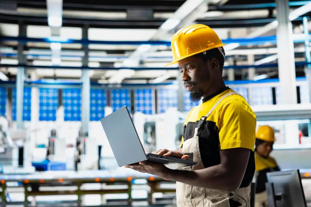Ouvrier en casque jaune consultant un ordinateur portable dans un atelier
