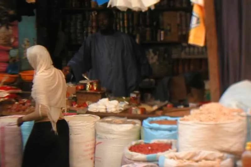 Épicier derrière son étal garni de sacs d'épices et de produits secs sur un marché au Sénégal