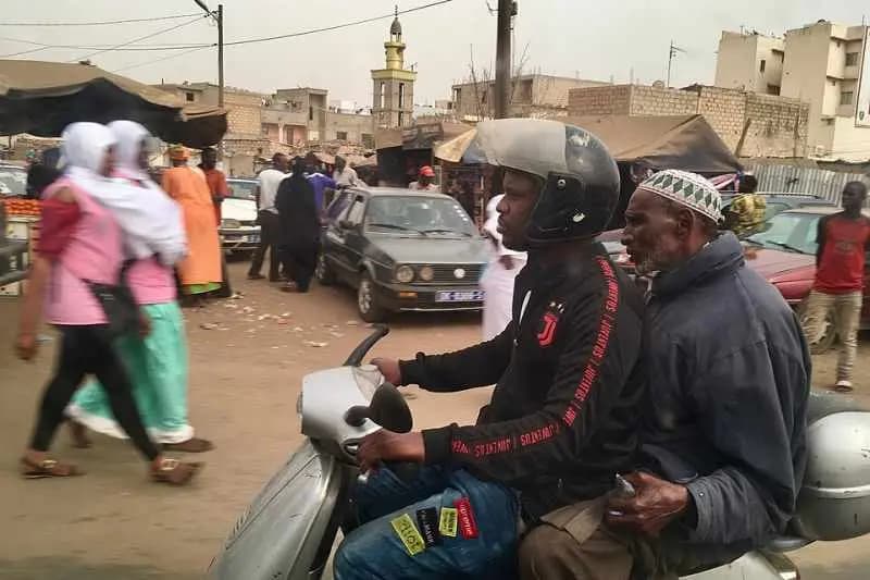 Un jeune homme en scooter emmène un homme âgé dans une rue animée d'un marché au Sénégal