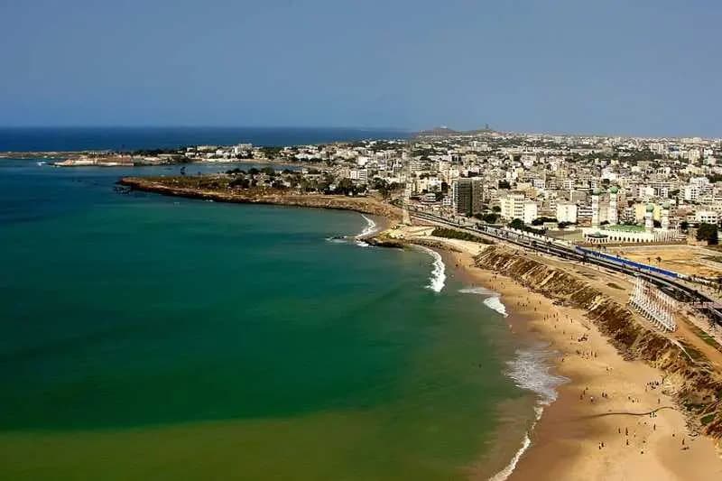 Vue aérienne de Dakar : la corniche, une plage de sable et les immeubles denses des quartiers de la Médina et du Point E