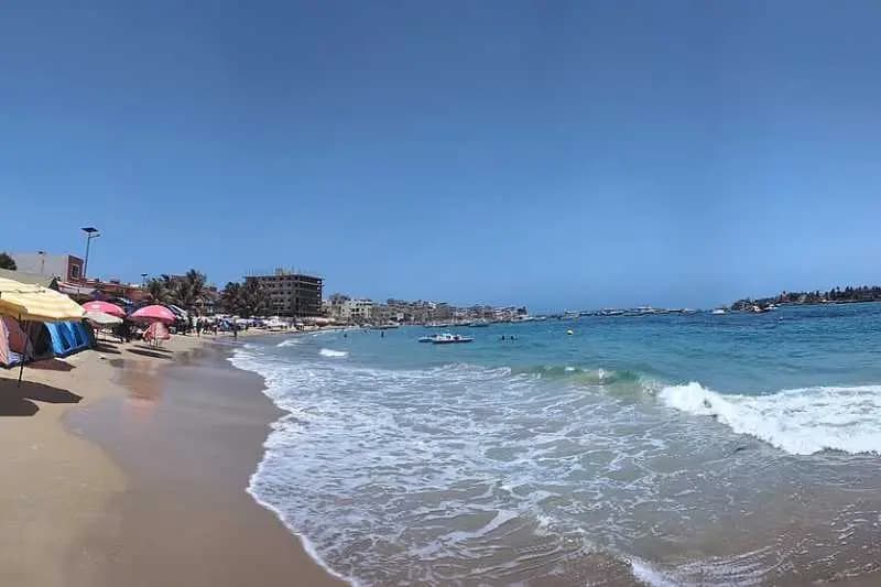 Plage de Ngor à Dakar par temps dégagé, avec parasols, baigneurs et pirogues sous un ciel bleu