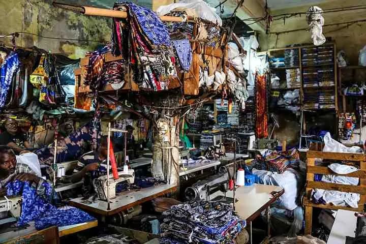Atelier de couture dans la Médina de Dakar : tailleurs à leurs machines, parmi les tissus imprimés accrochés aux murs