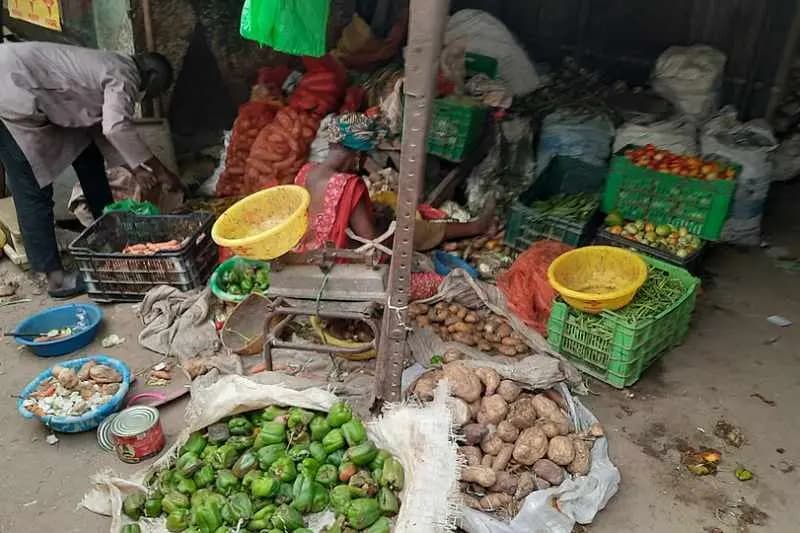 Étal de légumes au marché Moussanté de Thiès : légumes verts, tubercules et tomates dans des bassines et sur des sacs, avec une marchande penchée sur sa balance