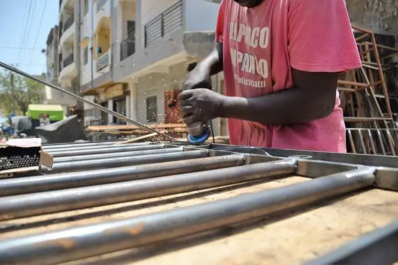 Artisan meulant des barres d'acier dans son atelier de menuiserie métallique au Sénégal
