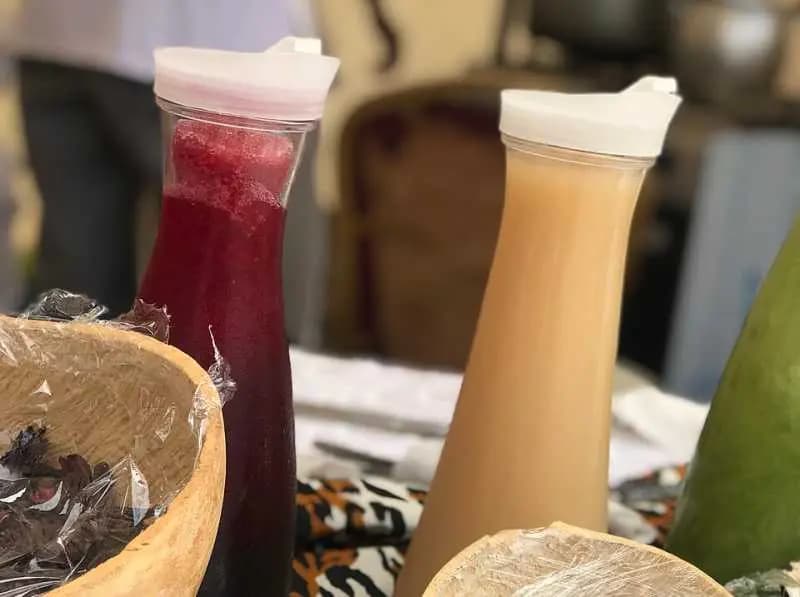 Deux carafes de jus locaux posées sur une table : bissap rouge foncé et bouye de couleur crème