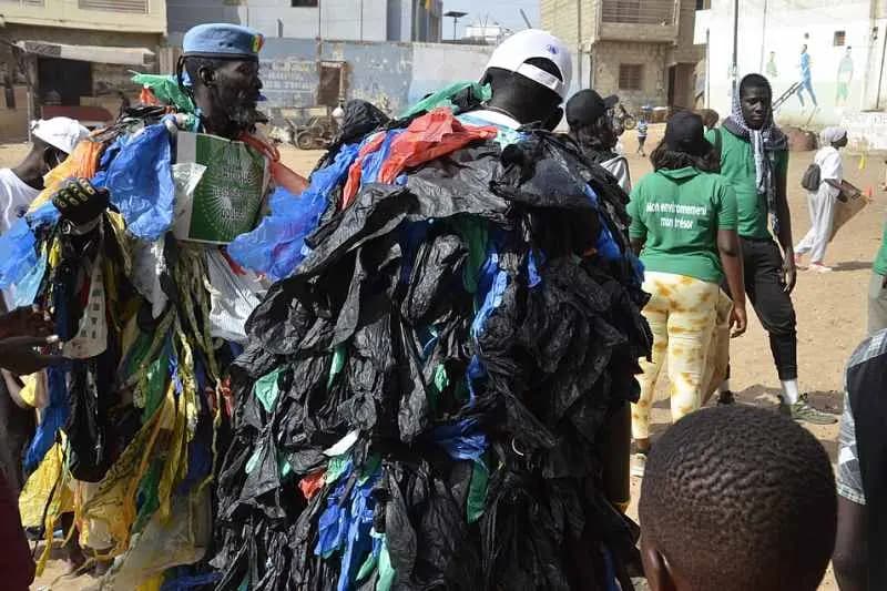 Homme vêtu d'un costume fait de sachets plastiques usagés noirs et colorés, entouré de passants dans une rue au Sénégal