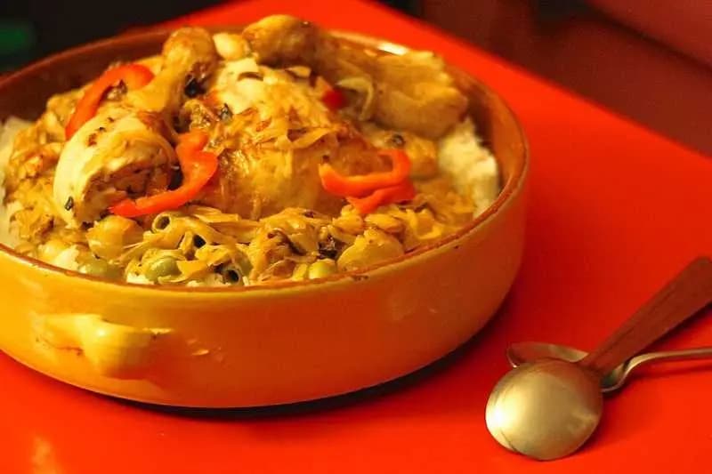 Plat de poulet yassa aux oignons et poivron rouge, servi sur du riz blanc dans un plat en terre