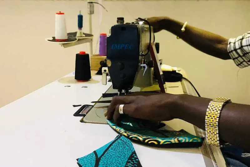 Mains d'un tailleur guidant un tissu wax sous l'aiguille d'une machine à coudre industrielle, dans un atelier de Hann Maristes à Dakar